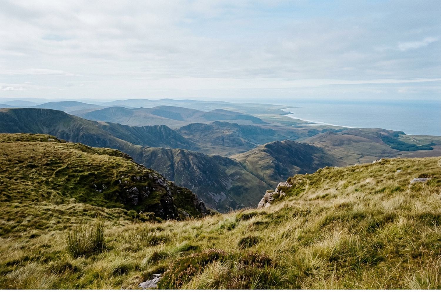 Green ridges falling away in layers toward a distant sea under a pale sky