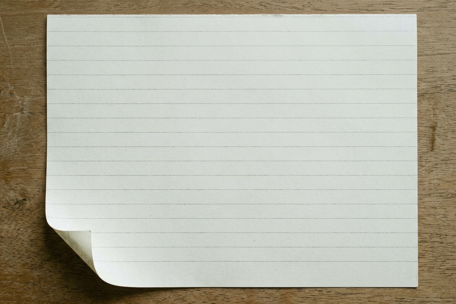 A blank sheet of pale ruled paper with one corner curling, lying flat