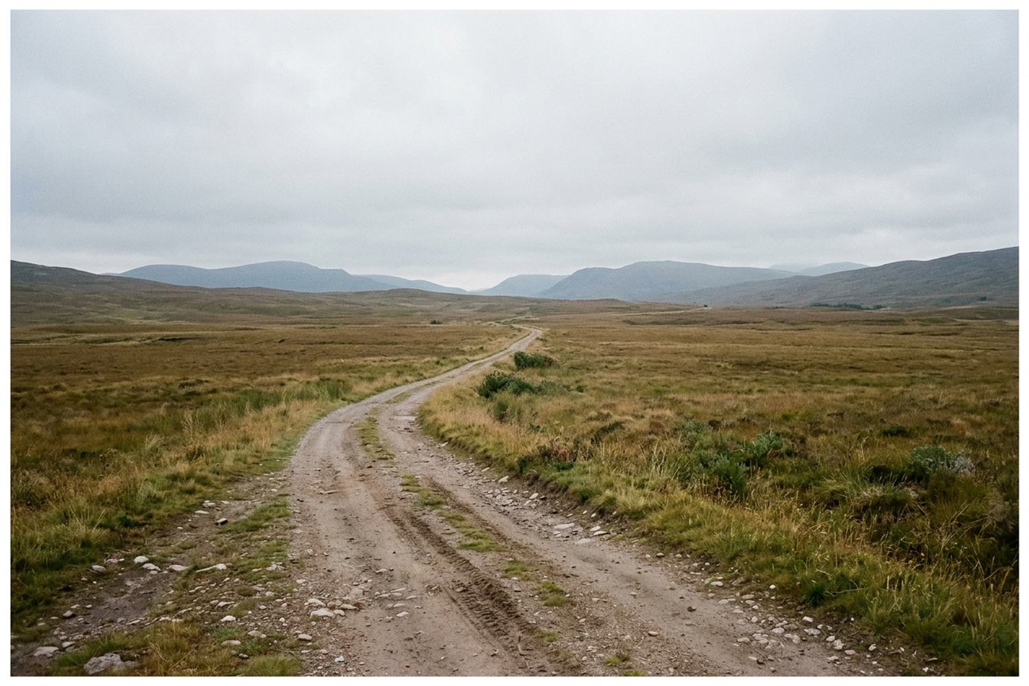 An unpaved track crossing wide open moorland toward low hills on the horizon