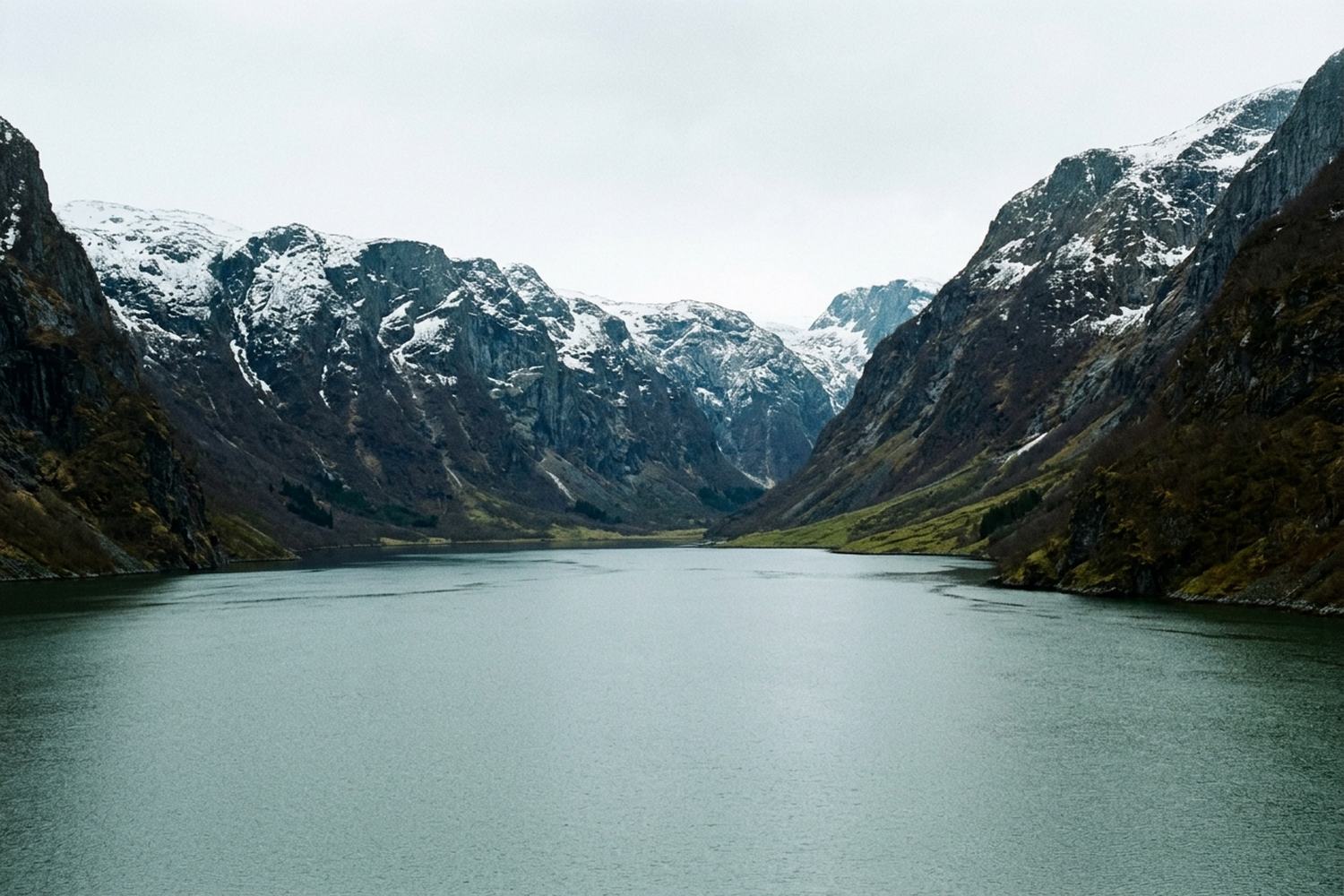 Still fjord water between steep cliffs with snow lying along the tops