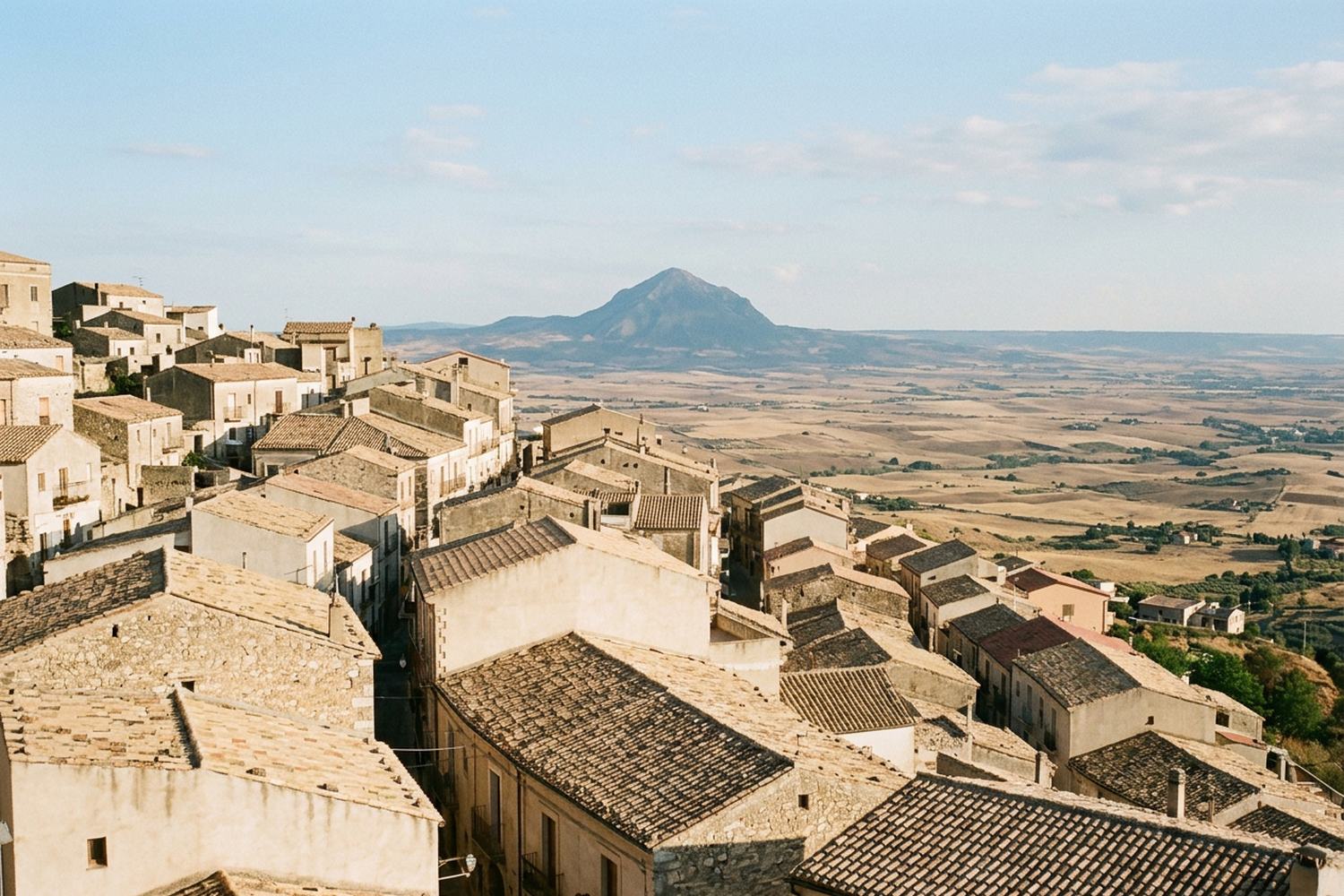 Tiled rooftops of a hill town above a dry plain, a conical mountain far off